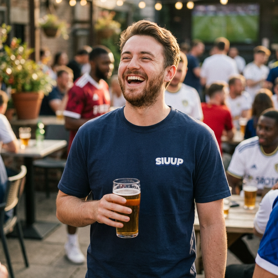 A man laughing at an outdoor pub holding a pint of beer, wearing a navy blue t-shirt with the white text 'SIUUP' on the chest.